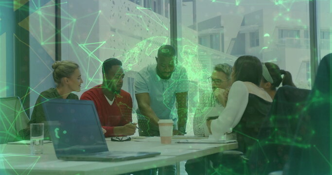 Team members leaning over laptop, documents, coffee cups around office table, with hologram globe