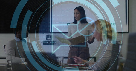 Presenting woman in blouse and skirt discussing report at conference table, with folder and screen
