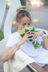 A young, beautiful girl with a bouquet of lilies of the valley on a walk.