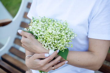 A young, beautiful girl with a bouquet of lilies of the valley on a walk.