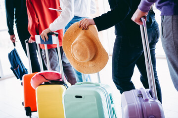 Travelers waiting in line at an airport holding suitcases and a straw hat on a sunny day showcasing...
