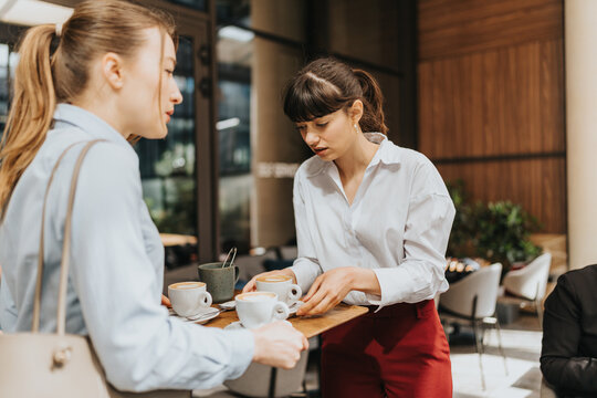 Two women in business attire having a conversation and coffee indoors.