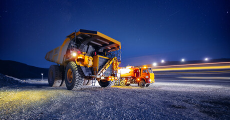 Fuel tanker car refueling large quarry dump truck in mining quarry, night work