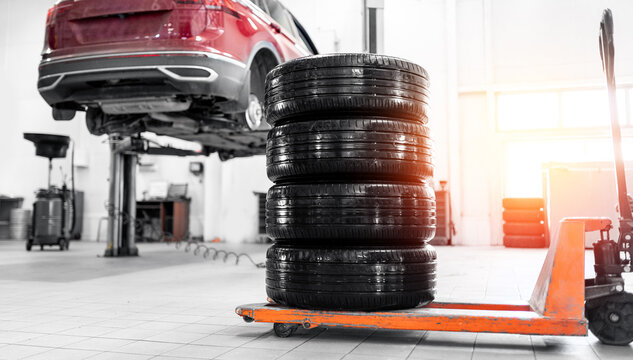 Car wheel service with stacked tires and elevated vehicle in auto workshop