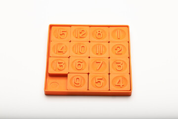 A 15-puzzle game in orange plastic. The puzzle consists of numbered tiles arranged in a 4x4 grid with one empty space for sliding tiles.