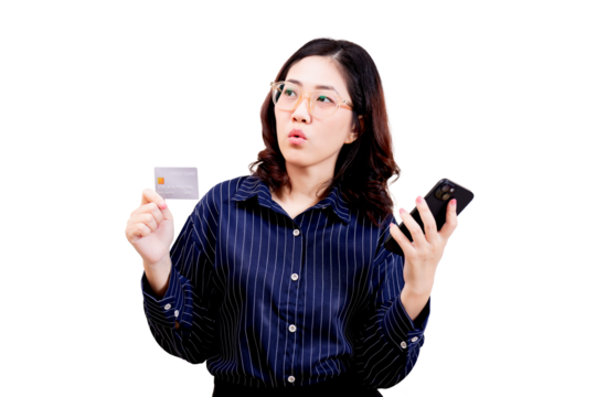 Asian young beautiful woman wearing glasses holds a credit card in one hand and a smartphone in the other, looking thoughtfully to the side.