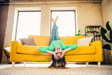 Young woman upside down on a vibrant couch in a modern loft apartment, playfully enjoying time in...