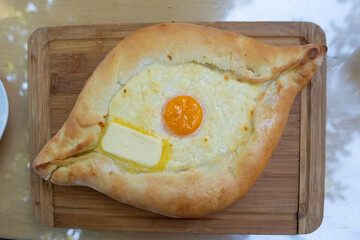 Traditional Georgian khachapuri Adjaruli with egg yolk and butter on wooden board, closeup view....