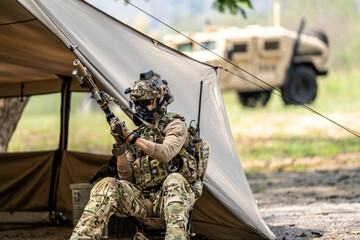 Special forces soldiers preparing tactical gear at military field base camp with weapons and...