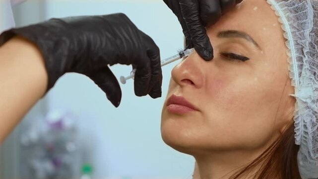 Injecting filler into nose bridge in aesthetic clinic. Administering dermal injection in nasal area for non-surgical correction. Performing cosmetic procedure using syringe for nose reshaping
