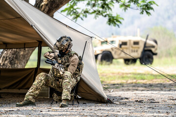 Special forces soldiers preparing tactical gear at military field base camp with weapons and...