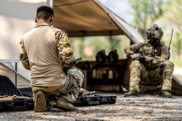 Special forces soldiers preparing tactical gear at military field base camp with weapons and...