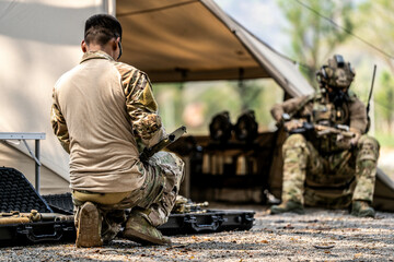 Special forces soldiers preparing tactical gear at military field base camp with weapons and...