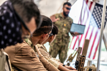 Soldiers resting and preparing inside military tent with American flag in background during...