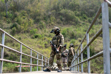 Tactical military team securing a bridge during field operation with soldier laying on ground and...