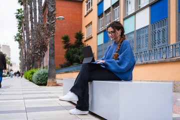University student using tablet while sitting on bench in city park