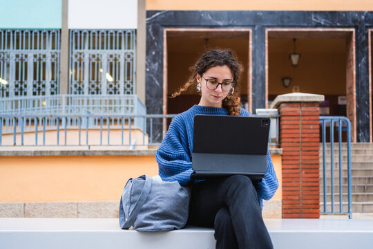 Focused student using digital tablet for online learning, enjoying fresh air and modern campus facilities