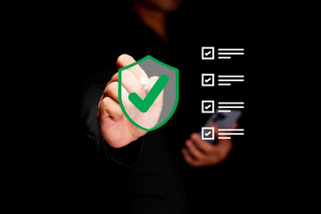 A person in black marks a green checkmark on a digital shield icon, symbolizing security and...