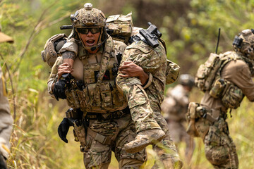 Fototapeta premium Soldier Carrying Injured Comrade During Tactical Combat Mission – Military Rescue Operation in Jungle, Armed Forces in Full Gear Providing Assistance Under Fire, Real Battlefield Scene