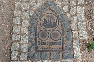 Pavement metal plaque. City called "Jewel of Pomerania" (Klejnot Pomorza) due to its rich collection of well-preserved medieval brick buildings and historic sites. Stargard, Poland.
