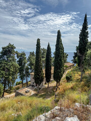 A peaceful stone building surrounded by tall cypress trees on a grassy hillside above the Ionian Sea in Parga, Greece.