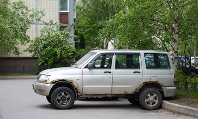 An old, light-colored, rusty SUV is parked near a residential building, Russian Avenue, Saint Petersburg, Russia, June 23, 2025