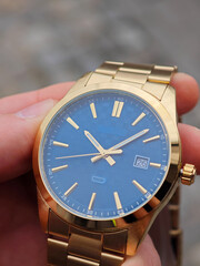 Close-up of a luxury gold wristwatch with a textured blue dial and date display, held in a man's...