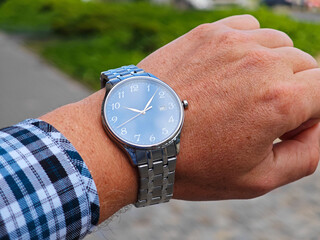 Elegant silver wristwatch with a deep blue face on a man's wrist in casual plaid shirt, showing the...