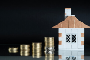 Coins stacked in a column with the dynamics of savings growth against the background of a house....