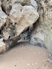 Coastal Cave: An evocative composition of weathered rocks, shaped by the sea's embrace, framing a shadowed cavern entrance and textured sand