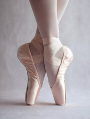 Close-up of ballerina's feet in pink satin pointe shoes on tiptoe, showcasing grace, balance and classical dance technique on a soft neutral background.