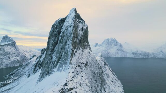 Segla auf der Insel Senja in Norwegen bei Sonnenuntergang im Winter, markante Felsformation vor klarem Himmel in kalter Lichtstimmung &uuml;ber schneebedeckter Fjord- und Berglandschaft