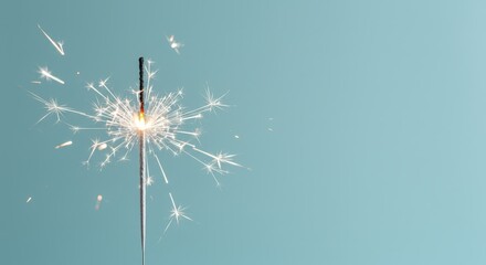 Obraz premium A burning sparkler casts bright sparks against a light blue background