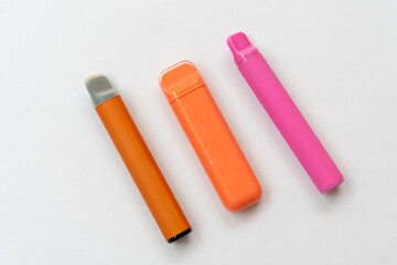 Three disposable electronic cigarettes in bright colors on a white background. Modern vape devices lying in a row.