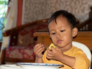 Close up of Toddler eating toast. Happy Asian toddler boy is having breakfast of toast with cheese and egg on his high chair. Toddler boy is having breakfast of toast on his high chair and table.