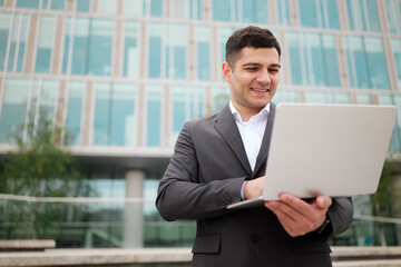 Business professional engages with laptop outdoors in a modern cityscape, showcasing a blend of technology and nature during a sunny day