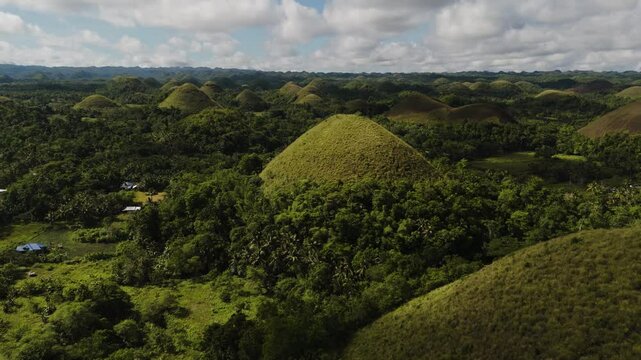 A lone majestic Chocolate Hill emerges from a thick green forest Among Dense Jungle in sunny cloudy day, Bohol, Philippines