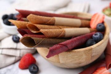Tasty fruit leather rolls and berries on white table, closeup