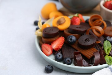 Tasty candied leather rolls, fruits and berries on white table, closeup. Space for text