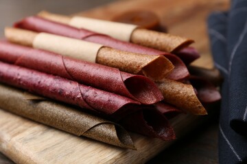 Tasty fruit leather rolls on wooden table, closeup