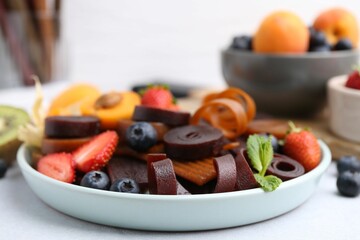 Tasty candied leather rolls, fruits and berries on white table, closeup