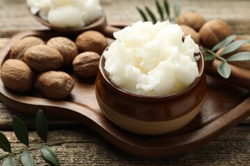 Natural shea butter, nuts and leaves on wooden table, closeup