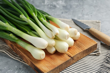 Fresh ripe green onions with cutting board and knife on grey textured table, closeup