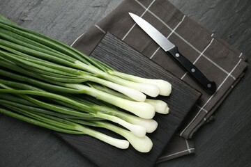 Fresh ripe green onions with cutting board and knife on black table, flat lay