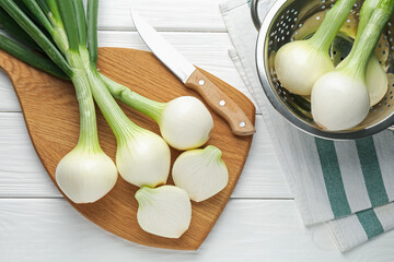 Fresh ripe green onions with cutting board and knife on white wooden table, flat lay