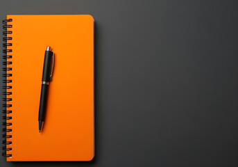 bright orange notepad and black writing pen on charcoal surface
