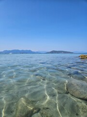 A beautiful view of the coast from a beach on an island in Greece, overlooking mountains and crystal clear water.