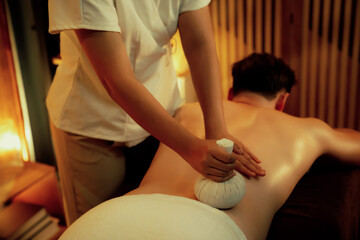 Hot herbal ball spa massage body treatment, masseur gently compresses herb bag on man body....