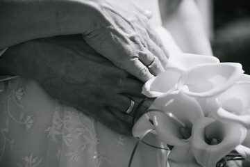 Close up of hands of bride and groom with rings and flowers