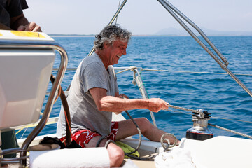 Senior man adjusting sail ropes while sailing in Costa Brava, Spain